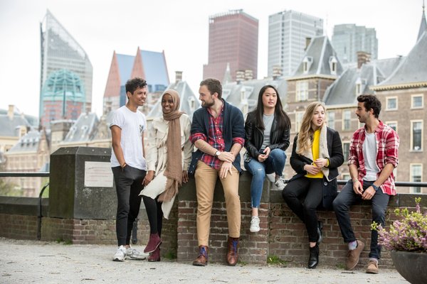 The photo shows a group of five diverse students in front of the skyline of The Hague, where Leiden University has a campus.