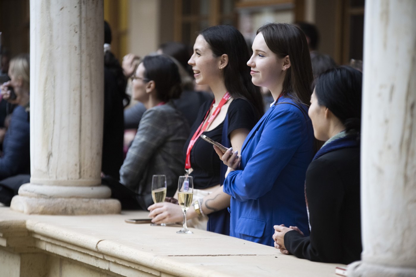 A few individuals engaged in conversation by a balcony, holding glasses of champagne, at a social or networking event.