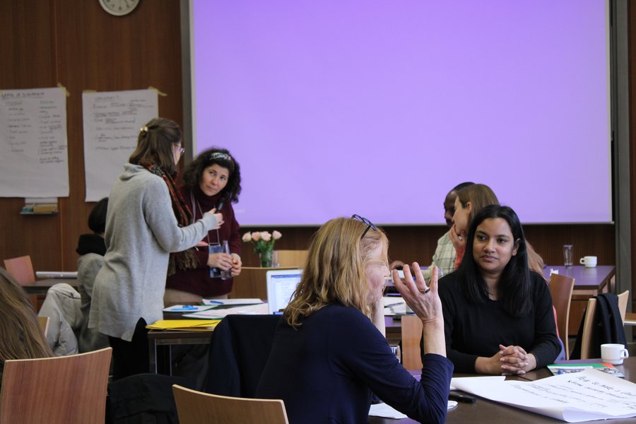 Workshop participants sit spread around several tables and talk.