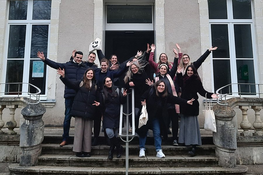 The picture shows the recipients of the EUniWell Research Thesis Prize with trainer Gabriele Hess-Fernandez on the steps in front of a building at Nantes Université. They are all raising their hands above their heads in joy.