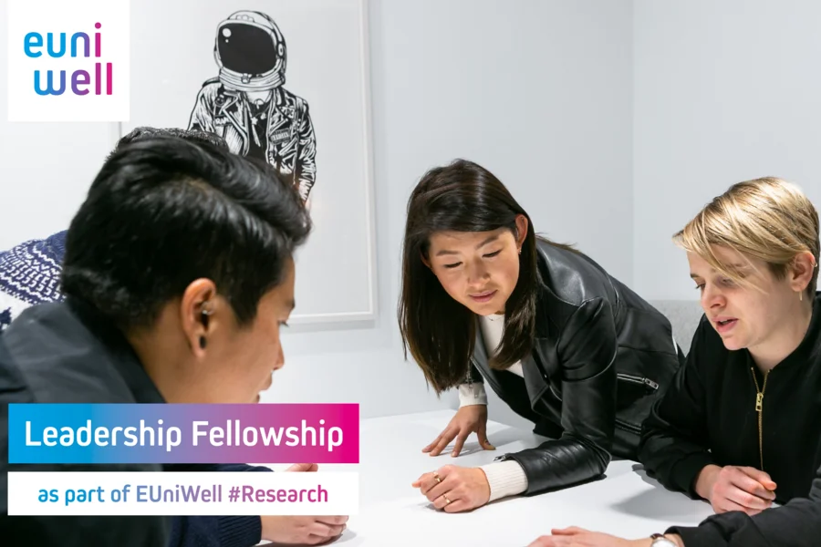 Four people working together at a table. In the upper left corner is the EUniWell logo, in the lower part of the picture stands the text: "Leadership Fellowship as part of EUniWell #Research".
