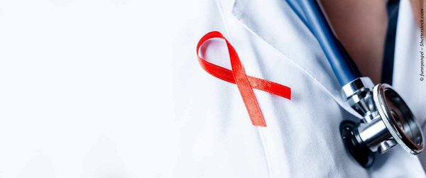 The photo shows a red AIDS ribbon attached to the lapel of a white doctor's coat. To the right you can see a stethoscope placed around someone's neck.