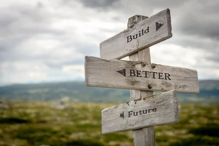 A wooden signpost with three directional arrows labeled "Build", "Better" and "Future" set in a landscape background, symbolising guidance or motivation towards improvement and progress.