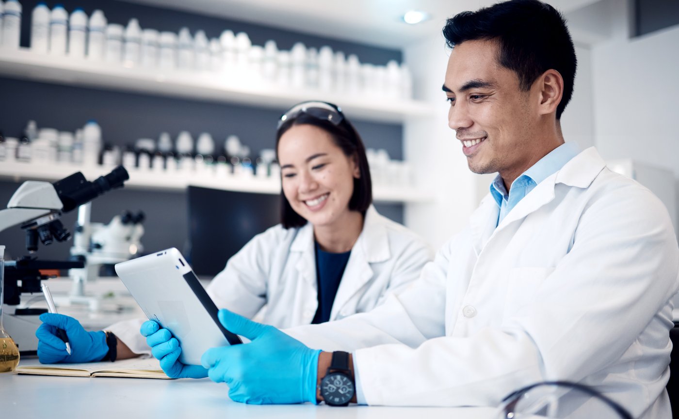 Two people in a science lab, looking at a tablet and smiling. 