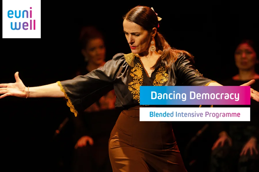 The image displays a female flamenco dancer in motion, wearing a traditional black outfit adorned with golden embroidery. Her expression is focused, and her pose captures the essence of the dance. Behind her, another performer is partially visible, suggesting a group performance. Overlaying the image is the logo for "EUniWell" and text that reads "Dancing Democracy" and "Blended Intensive Programme".