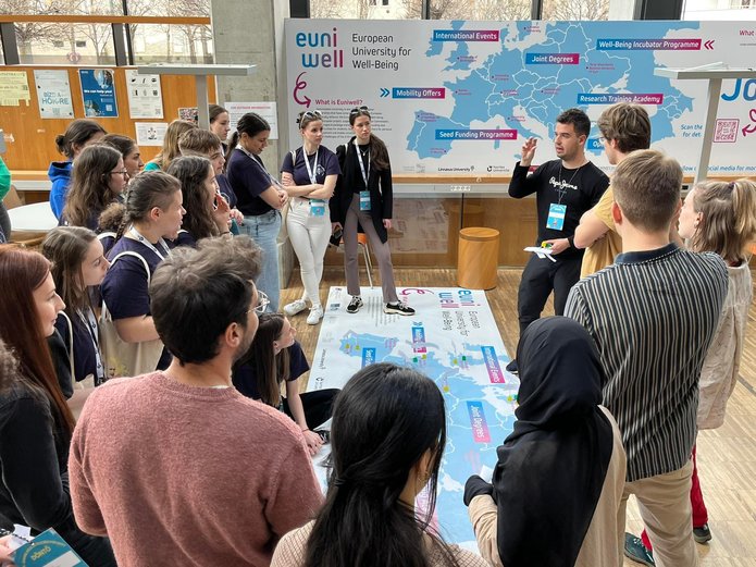 A group of students contemplate the EUniWell map lying on the floor. Another large EUniWell poster can be seen in the background.