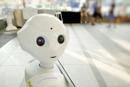 A white robot looking toward us, with people sitting in the background.