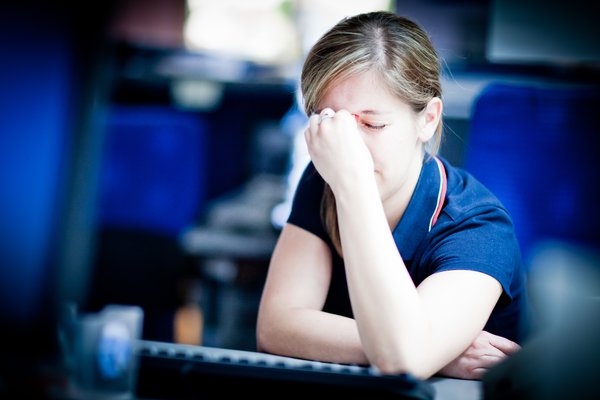a stressed woman sits in a lecture hall with her eyes closed 