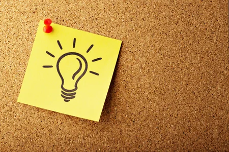 A sticky note with a light bulb drawn on it, on a corkboard