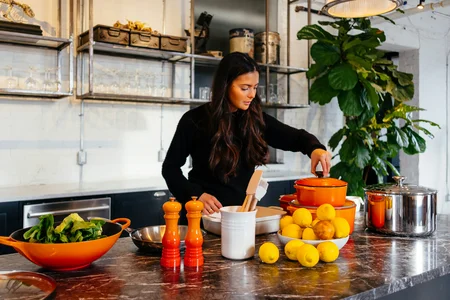 A woman in a kitchen preparing a meal with fresh vegetables and fruits