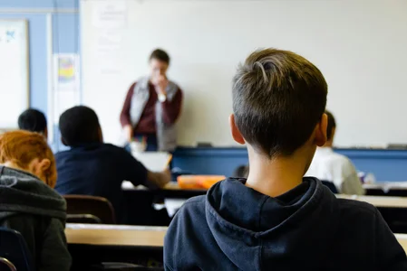 A picture of a classroom, with students listening to a teacher in the background
