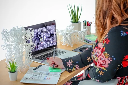 A woman scientist working in her office, writing a note while looking at her computer screen
