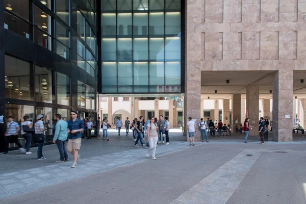 Students walking through the University of Florence campus courtyard, with modern university buildings and covered walkways in the background.