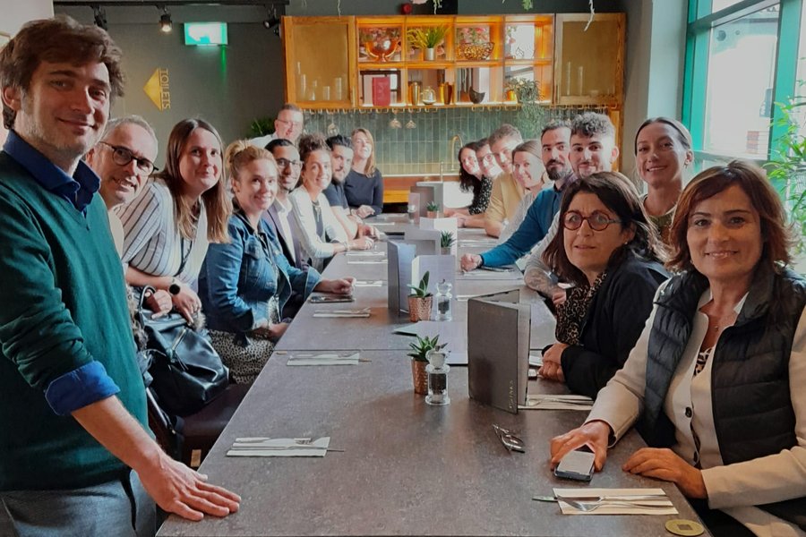Group of young entrepreneurs gathered around a long table at a modern restaurant, smiling and looking at the camera.